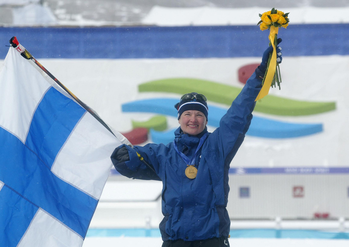 Kari nostaa kukkakimpun ja Suomen lipun ilmaan mitali kaulassaan palkintokorokkeella.